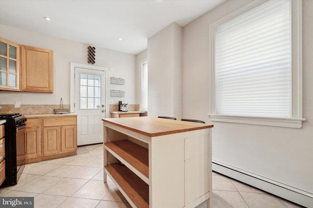 kitchen featuring a center island, black range oven, light tile patterned floors, baseboard heating, and light brown cabinets