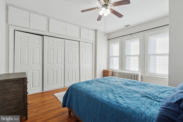 bedroom featuring a closet, hardwood / wood-style floors, radiator heating unit, and ceiling fan