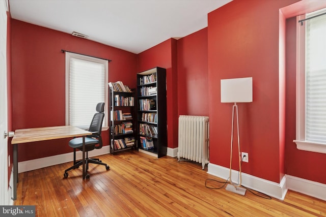 home office with a wealth of natural light, radiator, and wood-type flooring