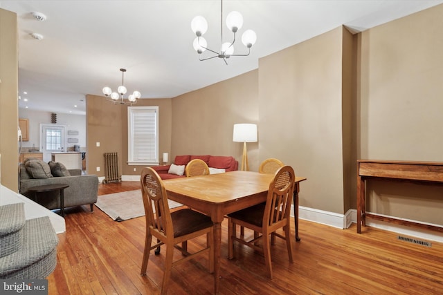 dining area featuring an inviting chandelier, light hardwood / wood-style flooring, and radiator heating unit