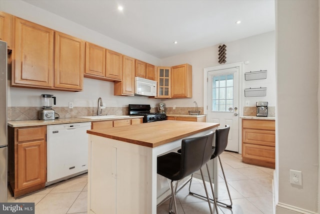 kitchen with white appliances, a center island, a breakfast bar, butcher block countertops, and sink