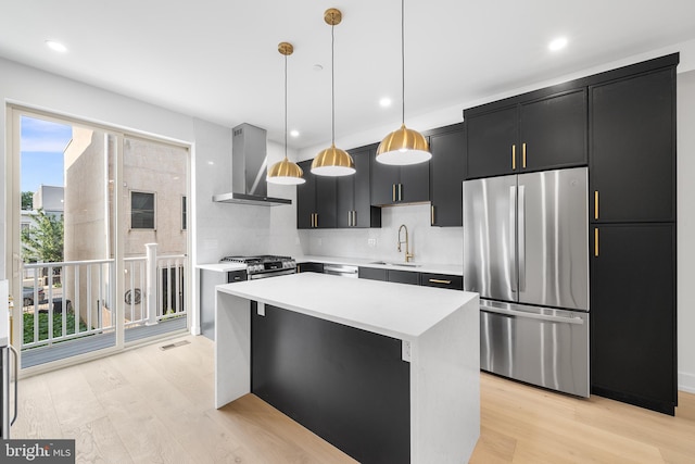 kitchen featuring stainless steel appliances, sink, wall chimney exhaust hood, a kitchen island, and pendant lighting