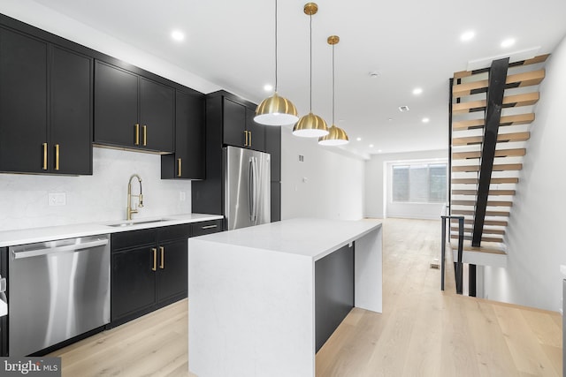 kitchen with stainless steel appliances, light wood-type flooring, a center island, pendant lighting, and sink