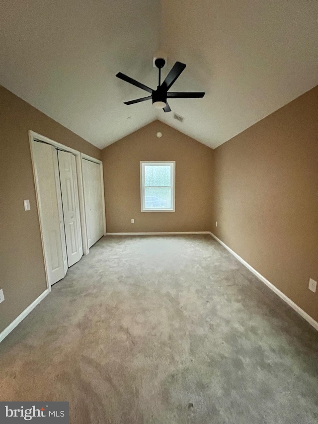 unfurnished bedroom featuring baseboards, carpet floors, visible vents, multiple closets, and lofted ceiling