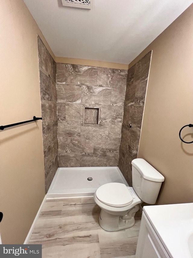 bathroom featuring toilet, tiled shower, vanity, and visible vents