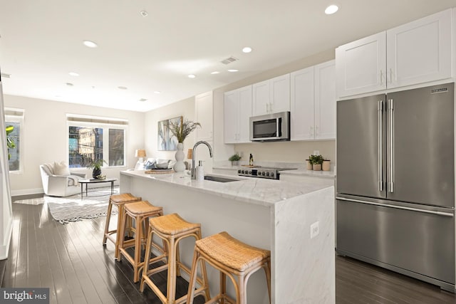 kitchen with appliances with stainless steel finishes, a kitchen island with sink, sink, and white cabinets