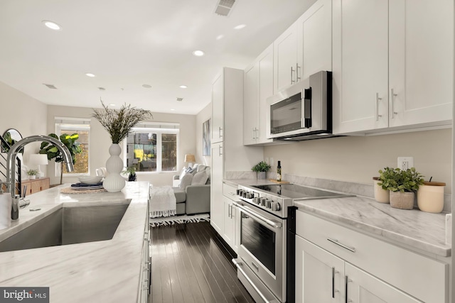 kitchen with sink, stainless steel appliances, dark hardwood / wood-style floors, light stone countertops, and white cabinets