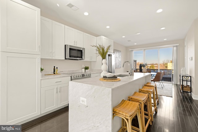 kitchen featuring stainless steel appliances, an island with sink, a breakfast bar area, and white cabinets