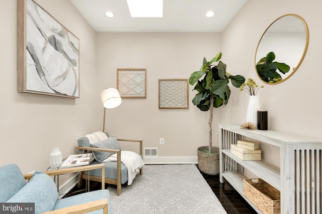 sitting room with dark wood-type flooring and a skylight