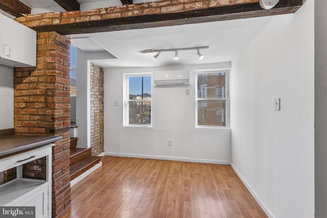 unfurnished living room featuring a wall mounted air conditioner, light hardwood / wood-style flooring, and track lighting