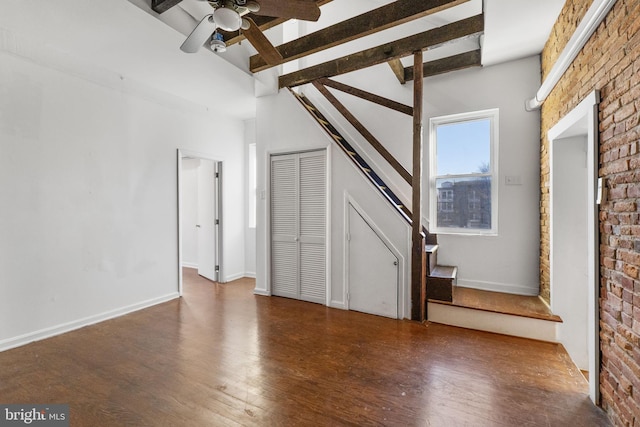 unfurnished living room with vaulted ceiling with beams, dark hardwood / wood-style floors, ceiling fan, and brick wall