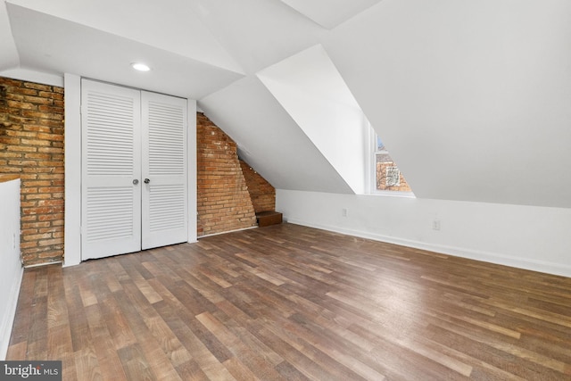 bonus room featuring dark hardwood / wood-style flooring, lofted ceiling, and brick wall