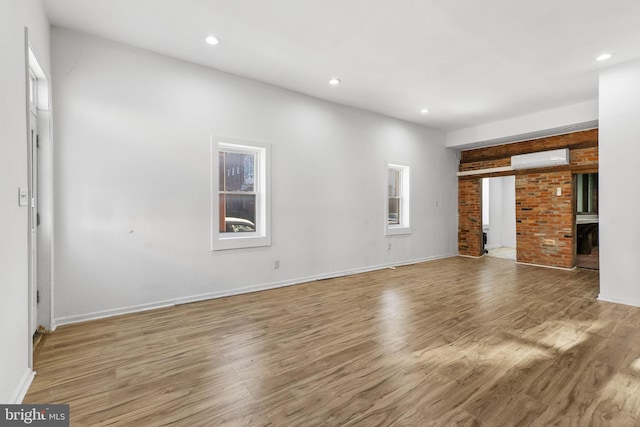 unfurnished living room with brick wall, a wall mounted air conditioner, and light hardwood / wood-style flooring