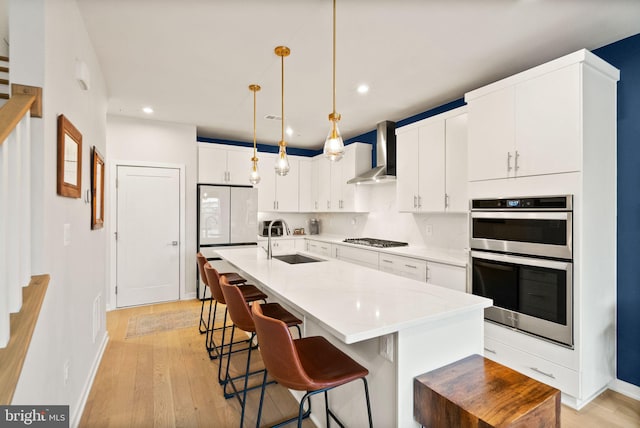 kitchen featuring white cabinetry, appliances with stainless steel finishes, wall chimney range hood, pendant lighting, and sink