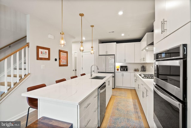 kitchen featuring white cabinets, appliances with stainless steel finishes, decorative light fixtures, a kitchen breakfast bar, and a kitchen island with sink