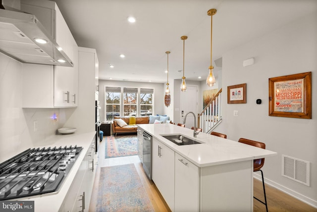 kitchen with decorative light fixtures, sink, stainless steel appliances, white cabinets, and wall chimney exhaust hood