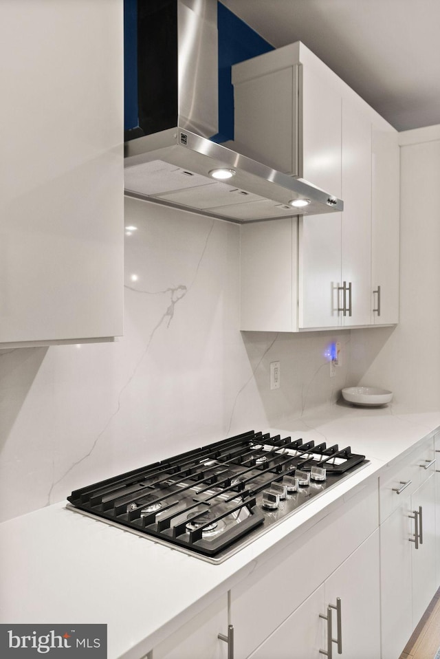 kitchen with stainless steel gas cooktop, decorative backsplash, white cabinets, and wall chimney range hood