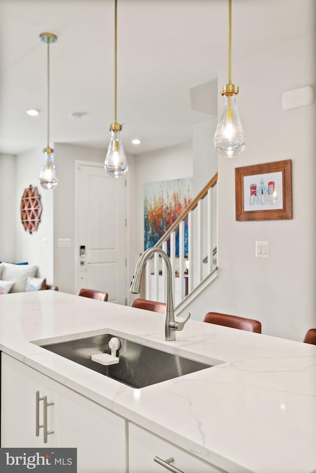 kitchen with white cabinets, light stone countertops, sink, and pendant lighting