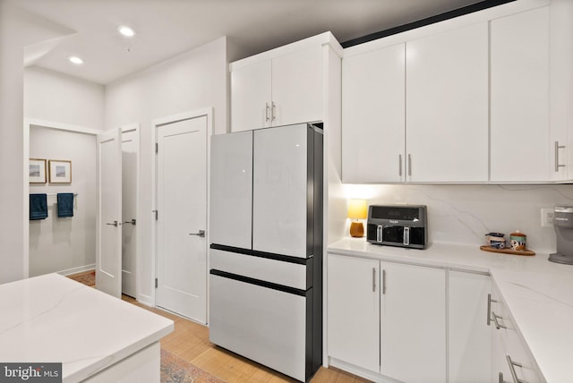 kitchen with refrigerator, decorative backsplash, white cabinetry, light wood-type flooring, and light stone countertops