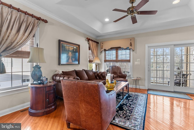 living room with ceiling fan, ornamental molding, a raised ceiling, and hardwood / wood-style floors