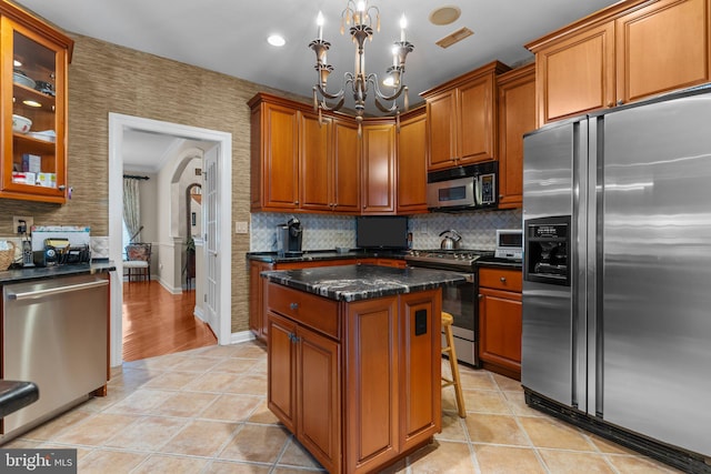 kitchen with light tile patterned flooring, a chandelier, a center island, dark stone countertops, and appliances with stainless steel finishes