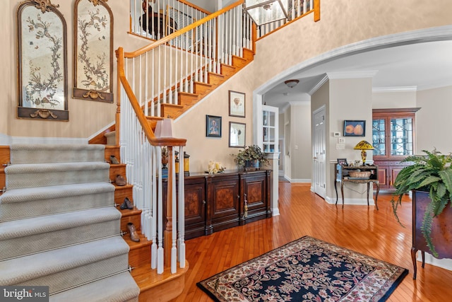 stairs featuring crown molding, hardwood / wood-style floors, and a high ceiling