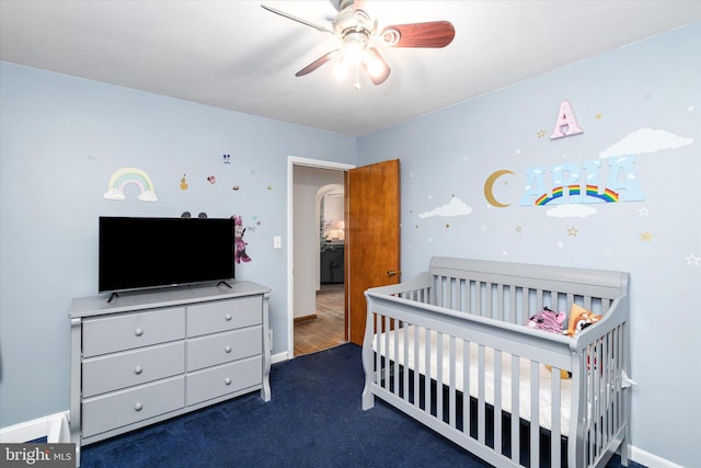 carpeted bedroom featuring a nursery area and ceiling fan