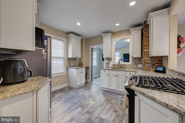 kitchen with sink, white cabinets, light hardwood / wood-style flooring, backsplash, and gas range