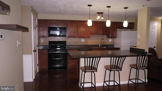 kitchen with sink, black appliances, pendant lighting, and a kitchen bar