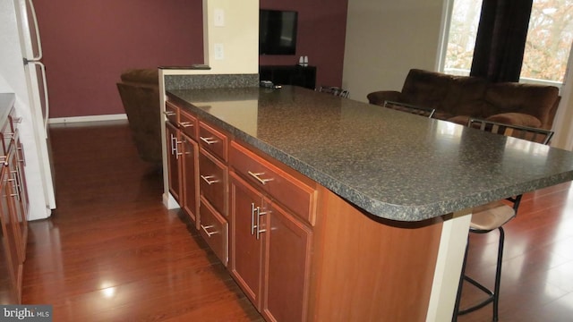 kitchen featuring white refrigerator, a breakfast bar area, a center island, and dark wood-type flooring