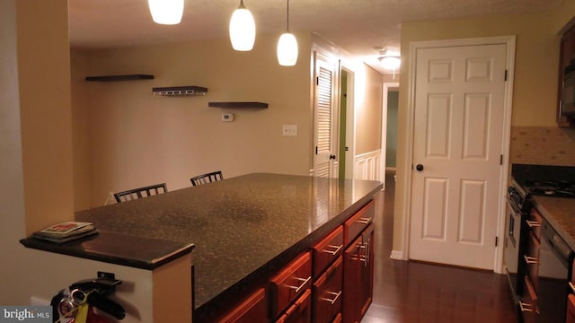 kitchen with a kitchen breakfast bar, hanging light fixtures, dark stone countertops, and stainless steel gas range oven