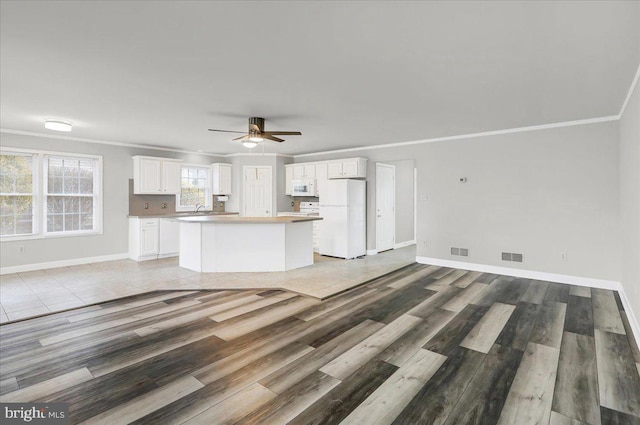 unfurnished living room featuring light wood-type flooring, ceiling fan, ornamental molding, and sink