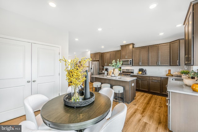 kitchen with stainless steel appliances, sink, a center island, a kitchen breakfast bar, and light hardwood / wood-style flooring