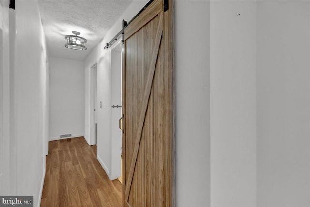 hallway with a textured ceiling, a barn door, and light wood-type flooring