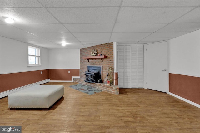 living room featuring a wood stove, a drop ceiling, baseboard heating, and light wood-type flooring