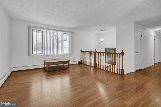 spare room featuring a textured ceiling, baseboard heating, and hardwood / wood-style floors