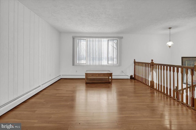 empty room with wood-type flooring, wood walls, and a baseboard radiator