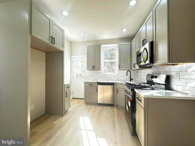 kitchen featuring sink, light wood-type flooring, decorative backsplash, gray cabinets, and appliances with stainless steel finishes