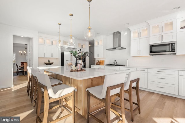 kitchen with white cabinets, appliances with stainless steel finishes, a center island, and wall chimney exhaust hood