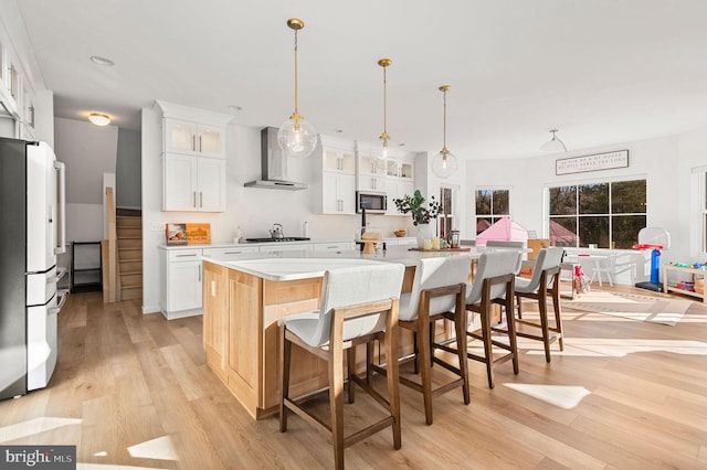 kitchen featuring fridge, wall chimney range hood, white cabinets, and a large island with sink