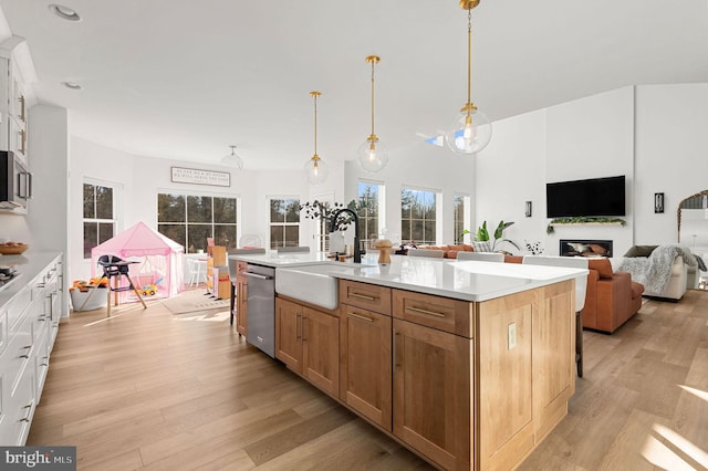 kitchen with a kitchen island with sink, white cabinets, hanging light fixtures, light hardwood / wood-style flooring, and sink