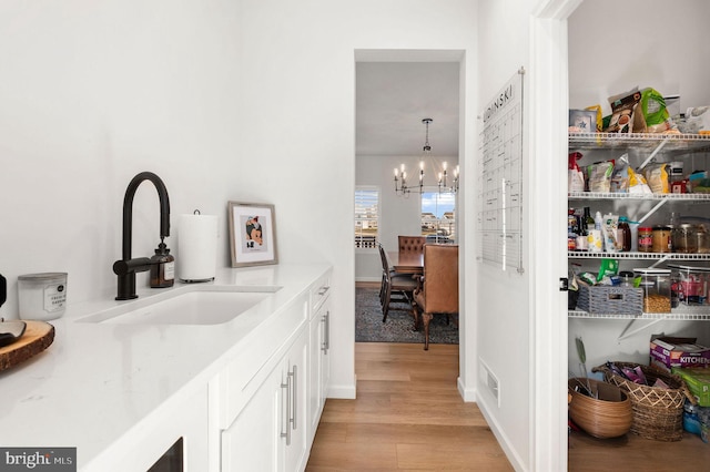 bar with white cabinets, decorative light fixtures, light hardwood / wood-style floors, sink, and a chandelier