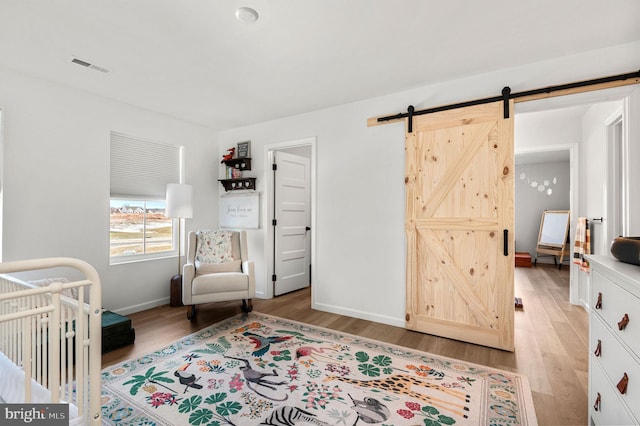 bedroom with light hardwood / wood-style floors, a barn door, and a nursery area