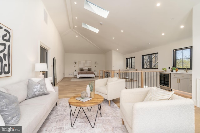 living room featuring light wood-type flooring, high vaulted ceiling, beverage cooler, recessed lighting, and a skylight