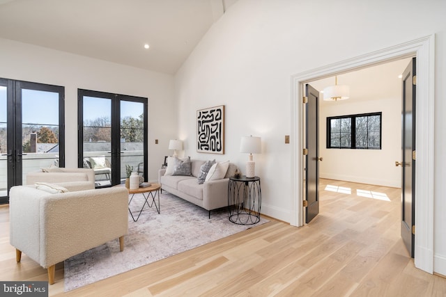 living area featuring high vaulted ceiling, french doors, light wood-type flooring, and a healthy amount of sunlight