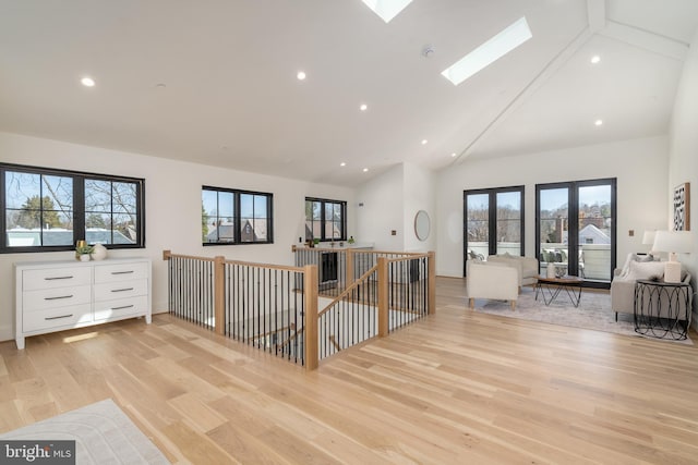 interior space featuring light wood finished floors, open floor plan, high vaulted ceiling, a skylight, and white cabinetry