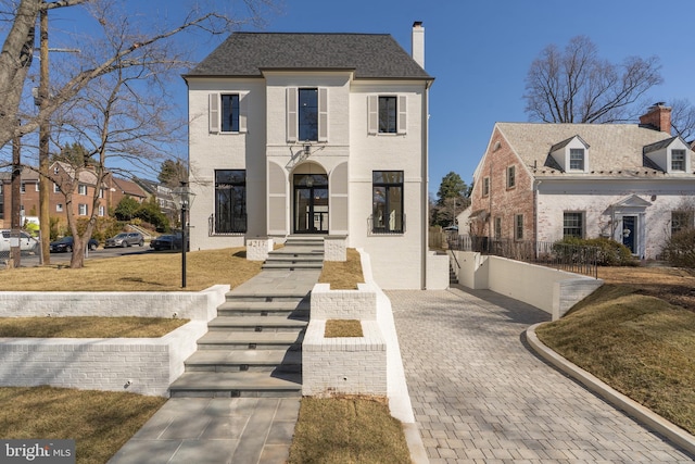 view of front of home featuring french doors, brick siding, a chimney, and a shingled roof