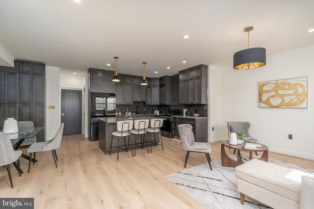 kitchen with stainless steel gas stove, a breakfast bar, backsplash, a center island, and light wood finished floors