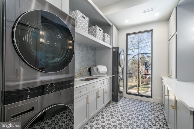 laundry area with stacked washer / dryer, visible vents, recessed lighting, cabinet space, and a sink