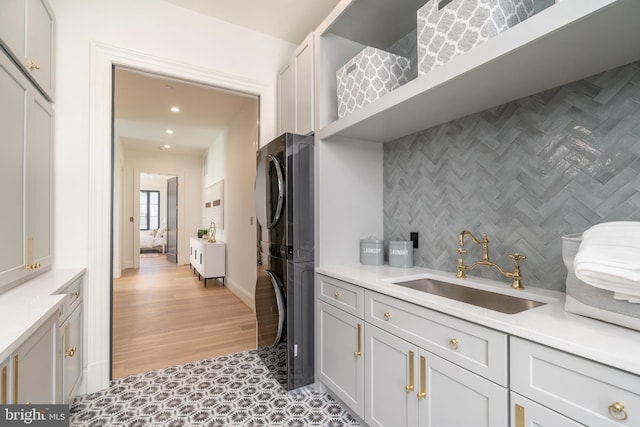 kitchen featuring a sink, decorative backsplash, light countertops, and stacked washing maching and dryer